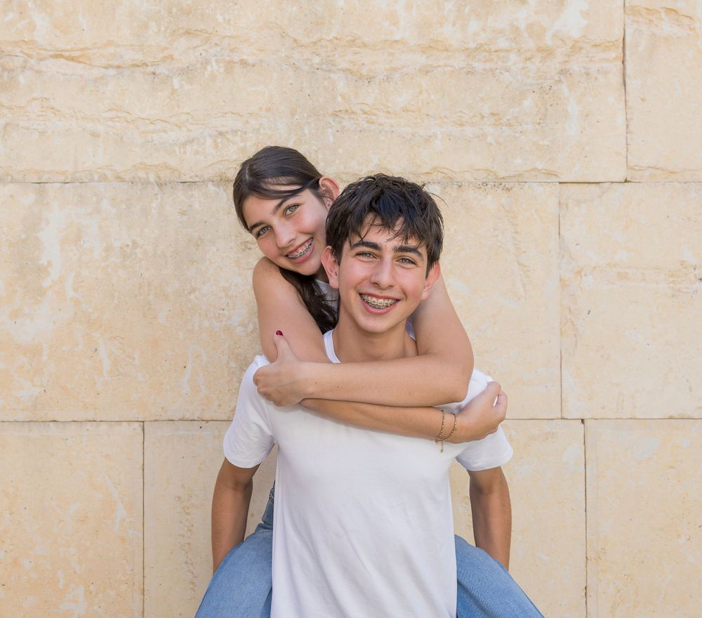 A piggyback ride moment against a beige stone wall backdrop.