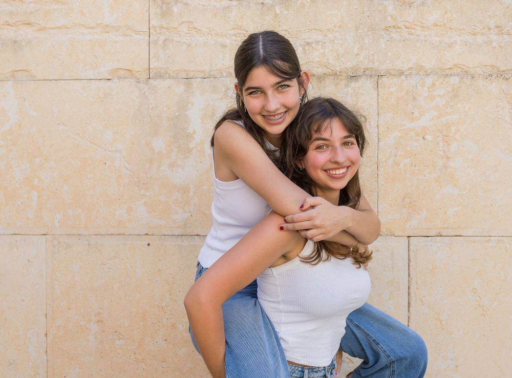 Two people sharing a playful hug against a light colored wall.