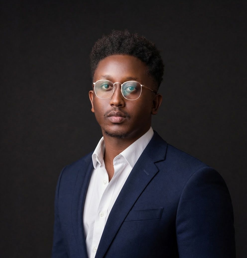 Professional headshot of someone wearing a black suit jacket and white button-down shirt against a neutral background.