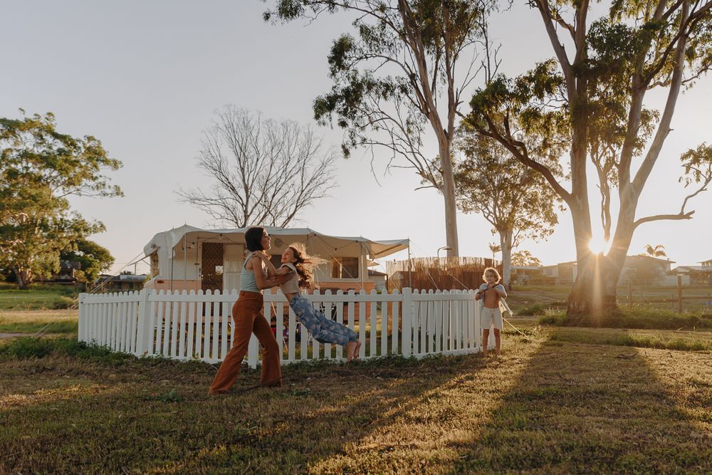 Mum twirling daughter in afternoon sun in front of vintage caravan