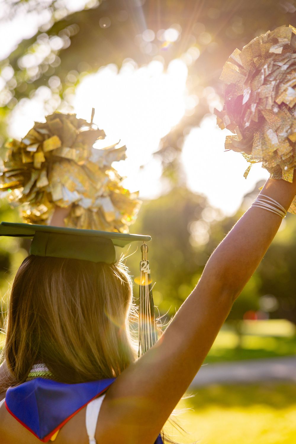 Graduate in cap and gown holding up bouquet against sunset backlight.