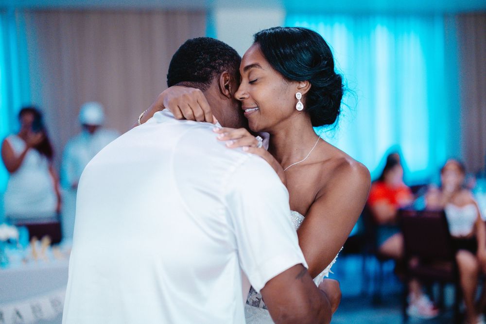 A bride and groom share an intimate first dance embrace at a wedding reception with blue lighting.