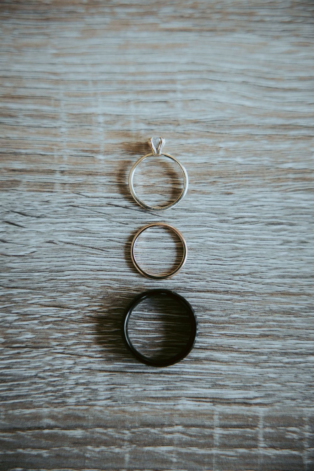 Three wedding rings arranged vertically on rustic wooden surface, including diamond engagement ring.