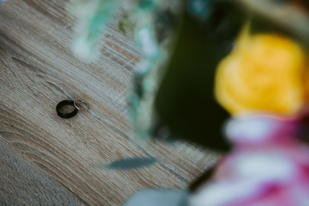Single wedding band ring resting on wooden surface with colorful floral bokeh background.