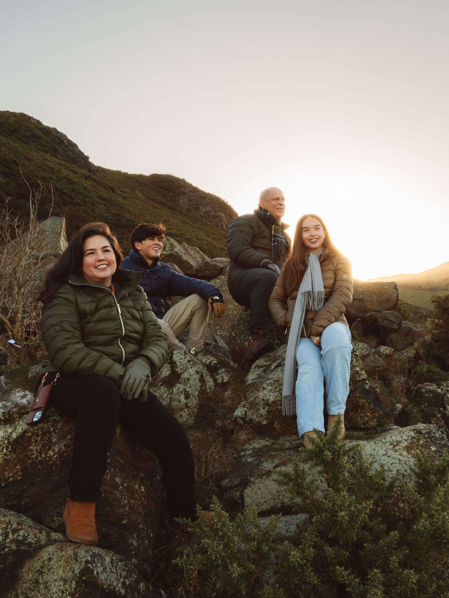 Friends sitting together on coastal rocks during golden hour sunset.