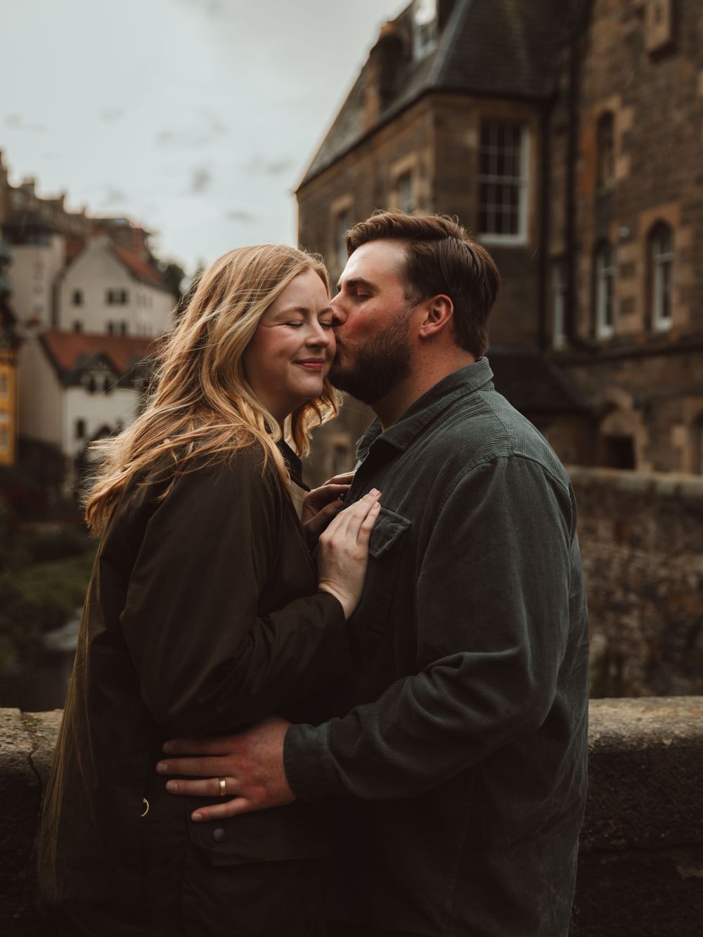 Romantic couple sharing intimate moments against historic stone building backdrop.
