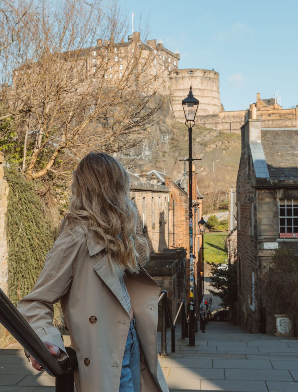 Person in beige coat walking through historic Edinburgh streets with stone buildings.