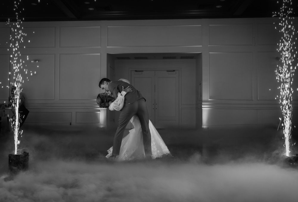 Black and white wedding photo of couple sharing first dance with sparkler fountains and dry ice fog on elegant ballroom floor.