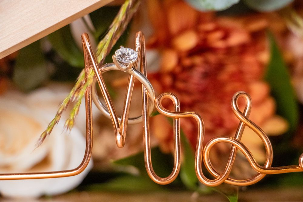 Gold wire 'Mrs' text decoration with diamond engagement ring displayed.