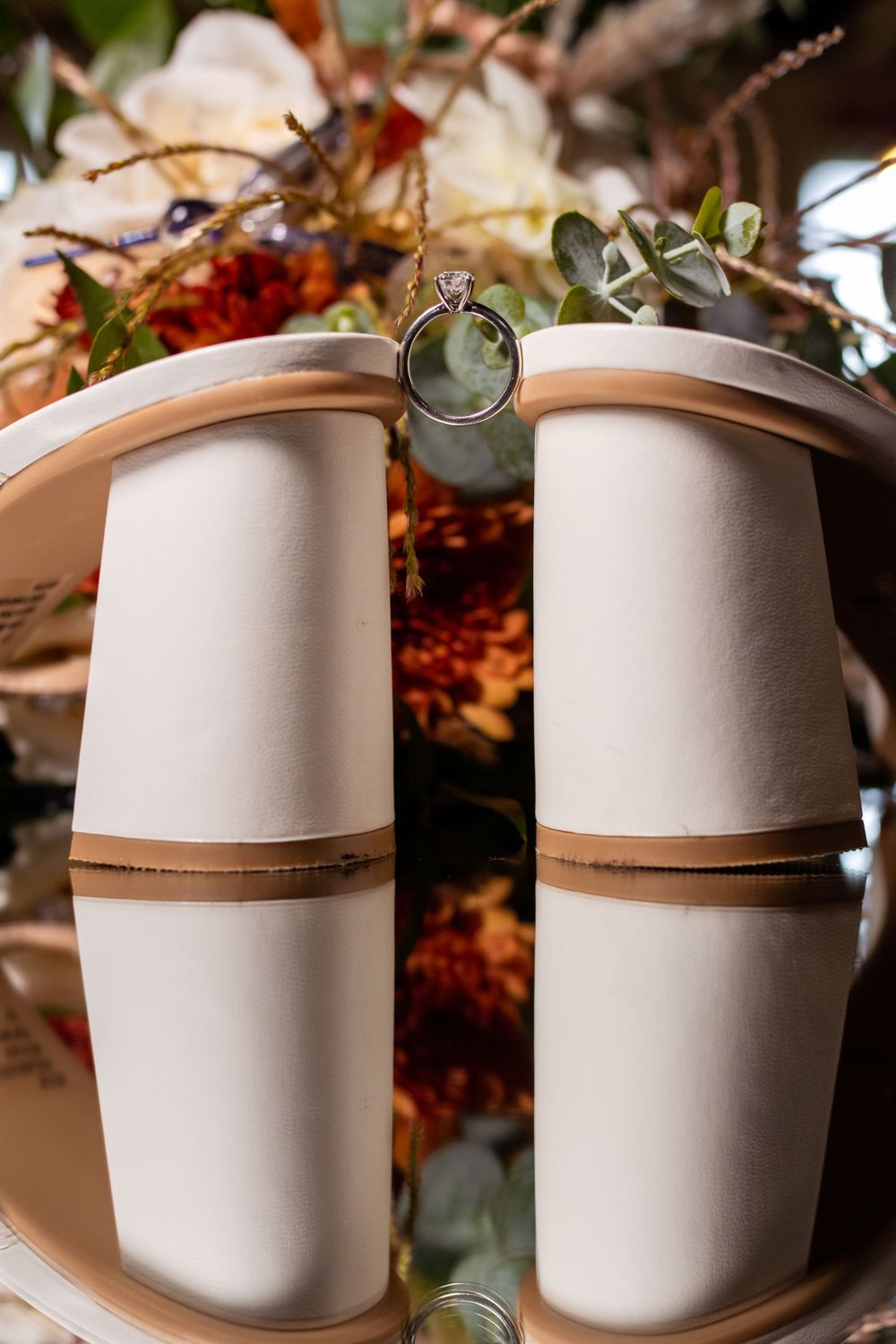 White ceramic vases with brown accent bands arranged on a table with floral decor and greenery.
