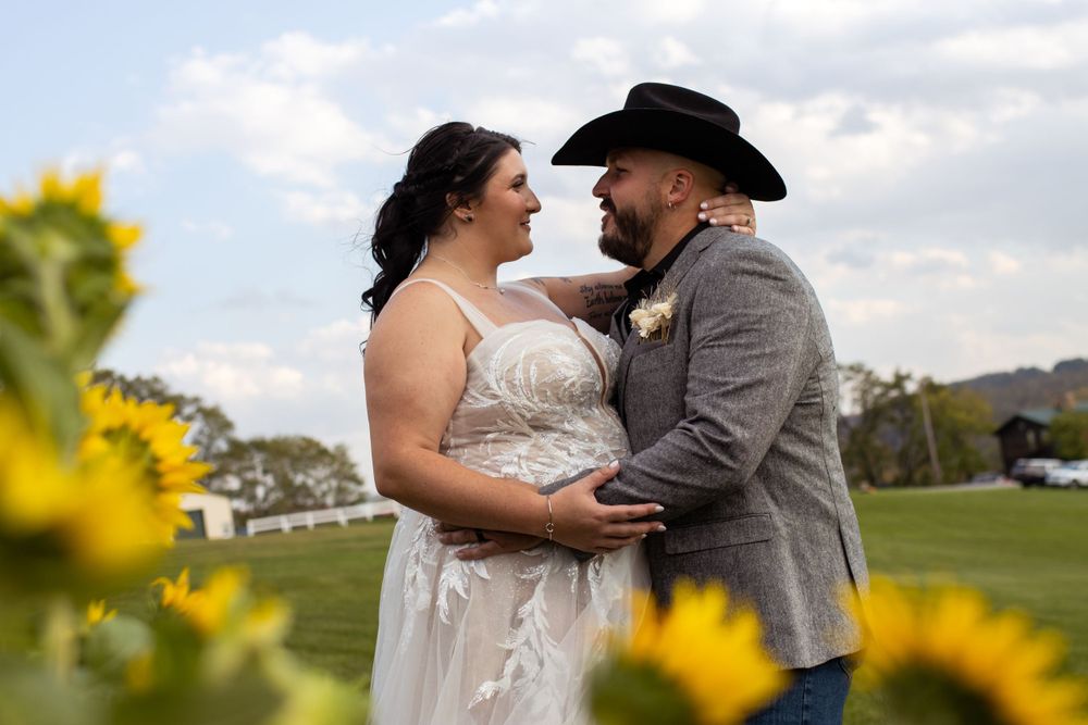 Couple shares romantic moment in sunflower field wearing wedding attire during outdoor countryside celebration.