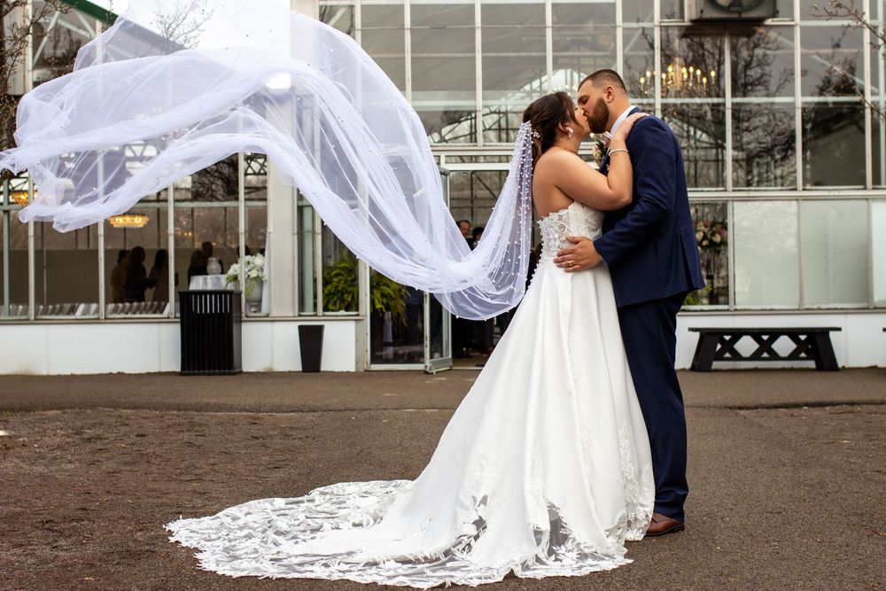 A romantic outdoor wedding moment catches the elegant flow of a lace veil in the breeze.