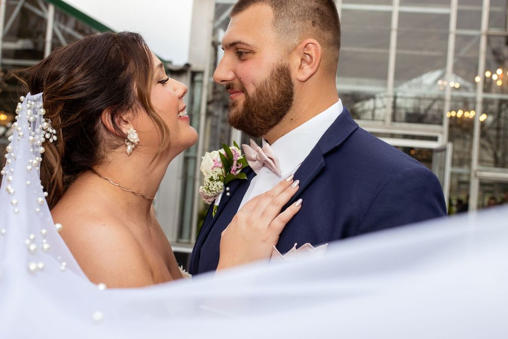 A romantic wedding moment with bride and groom sharing an intimate pose under the veil outdoors.
