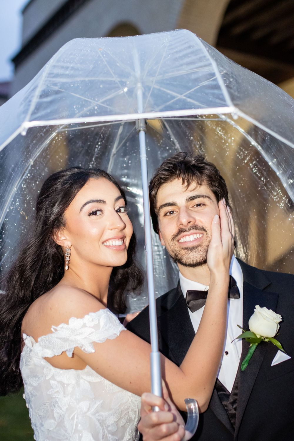 A couple shares an intimate moment under a clear umbrella on their wedding day.