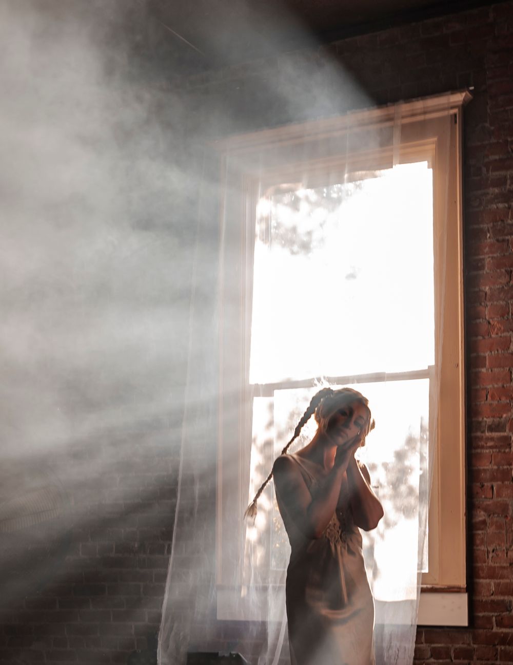 Atmospheric portrait with sunbeams and smoke effects through window.
