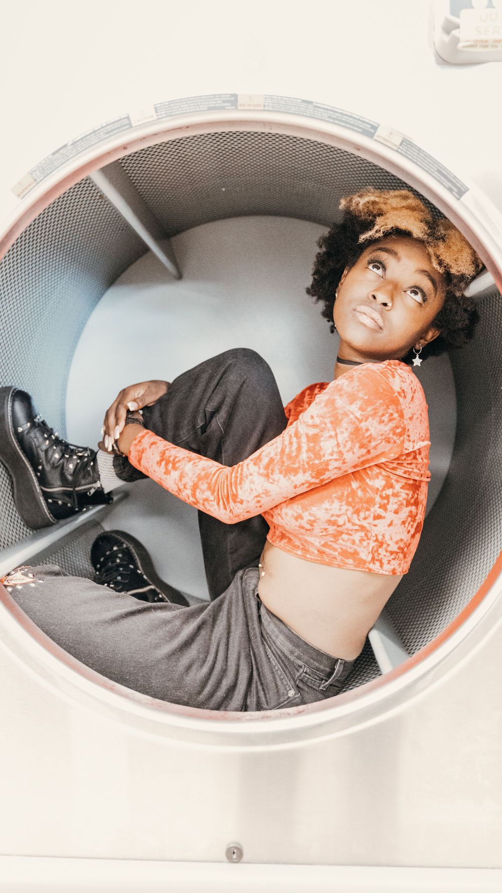 Dynamic photo of someone in orange crop top and jeans playfully posing inside industrial circular frame.