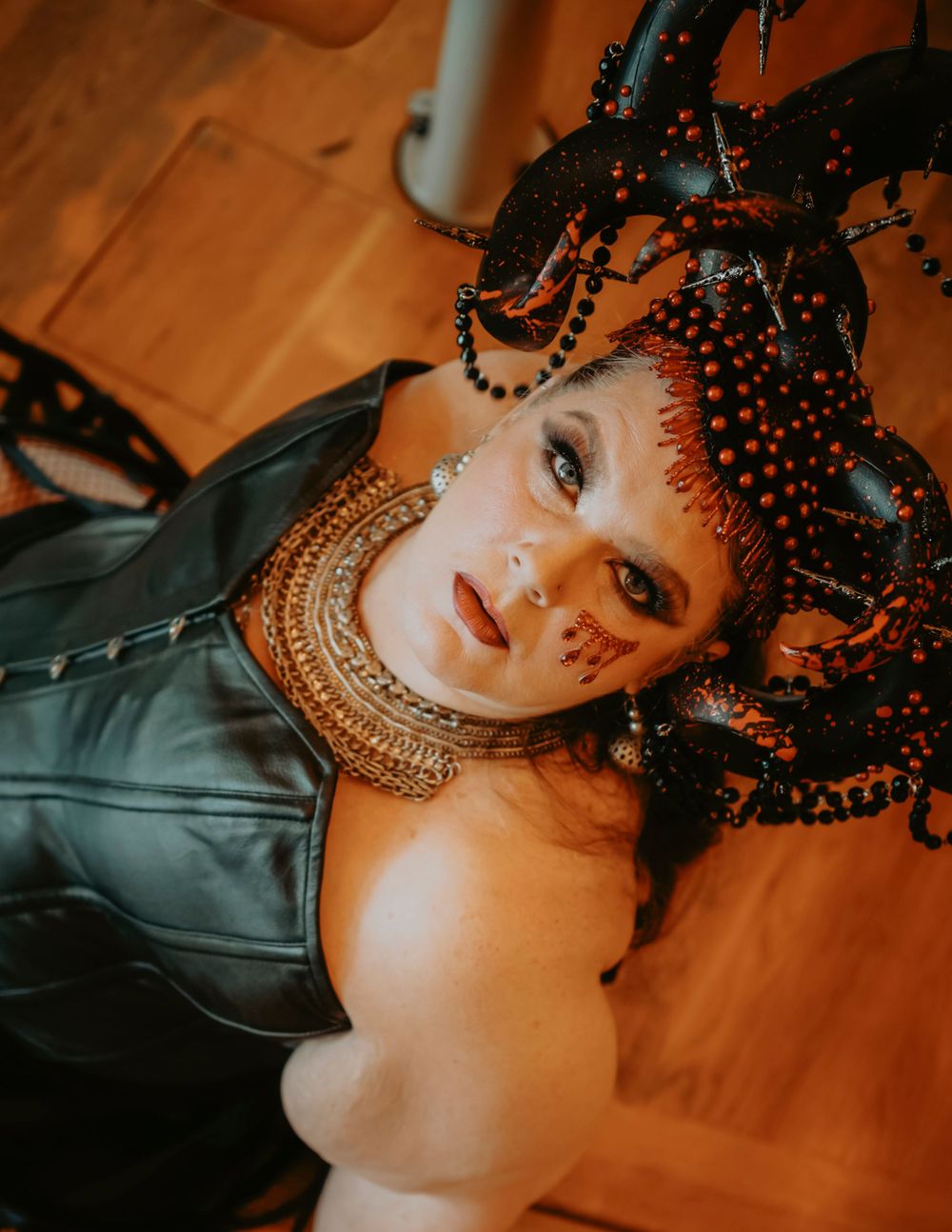 Close-up portrait showing intricate face paint, beaded headdress and metallic corset in gothic style.