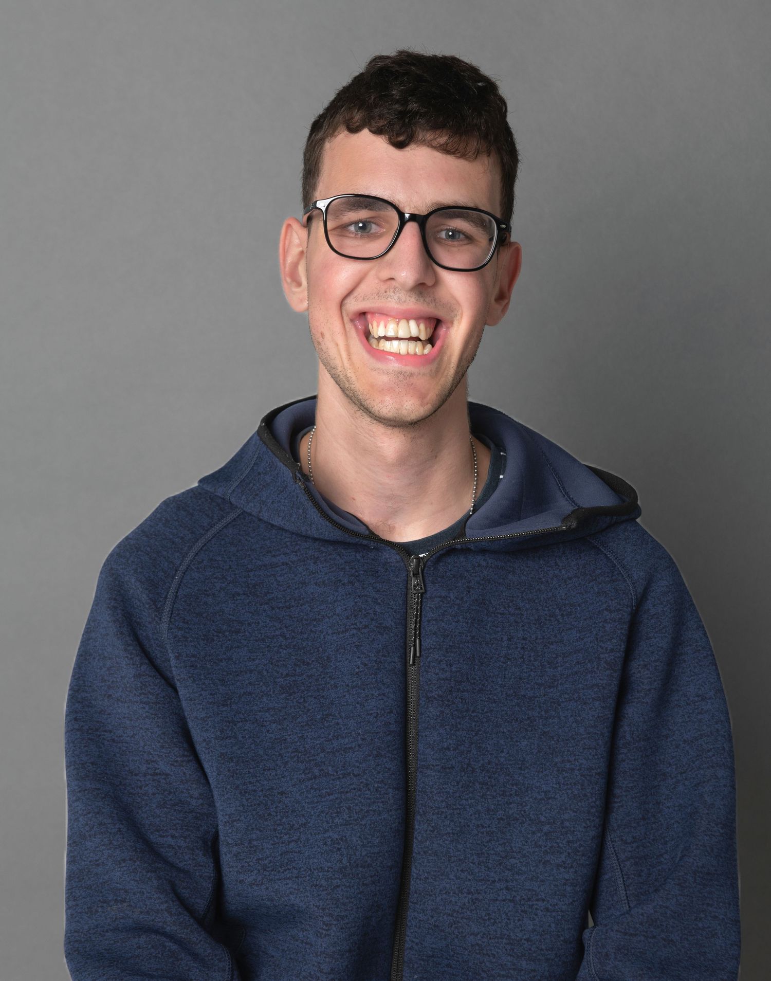 Portrait of photographer in blue hoodie smiling against grey studio background.