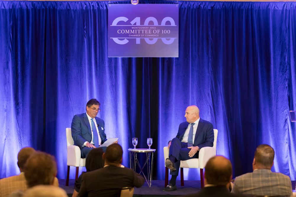 Two speakers engage in fireside chat discussion on stage with C100 banner backdrop.