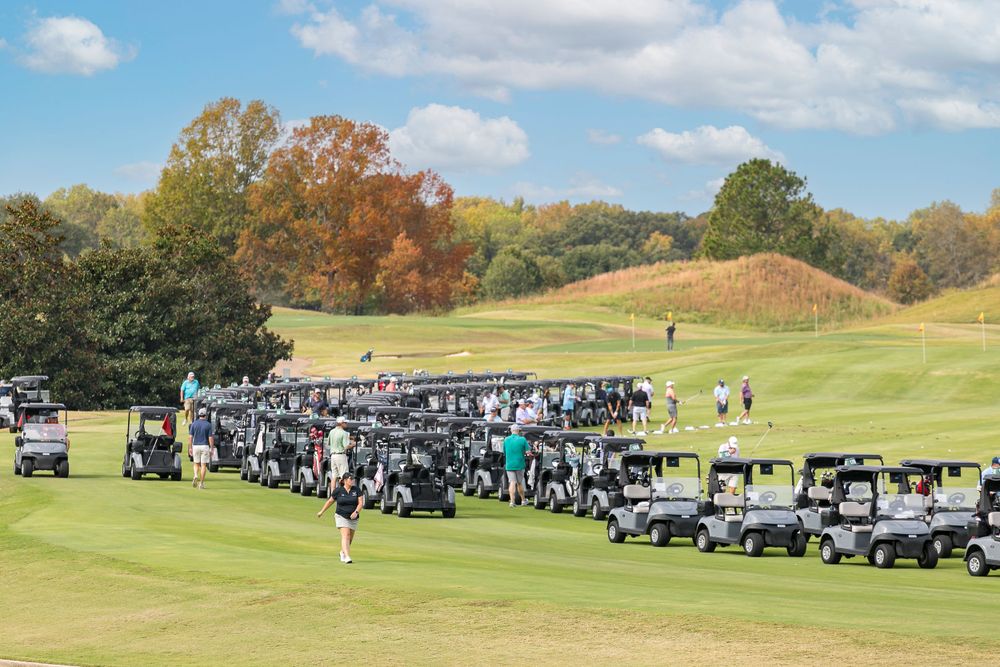 Long line of golf carts on course during autumn tournament with colorful fall foliage.