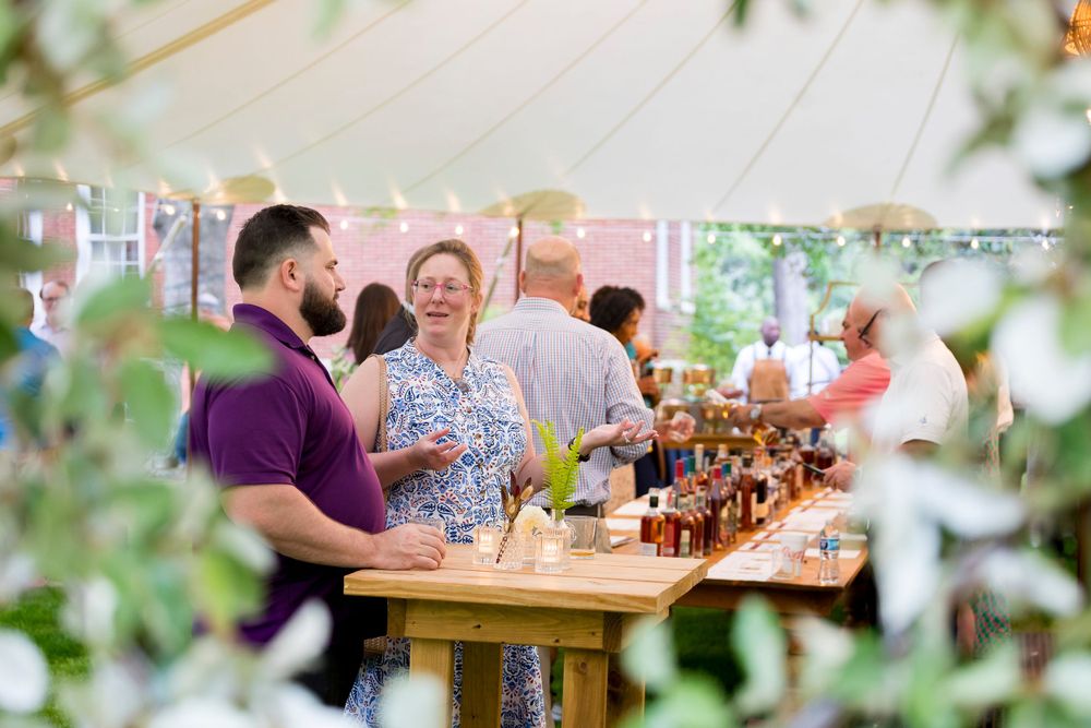 People enjoying drinks and conversation under a tent at an outdoor event.