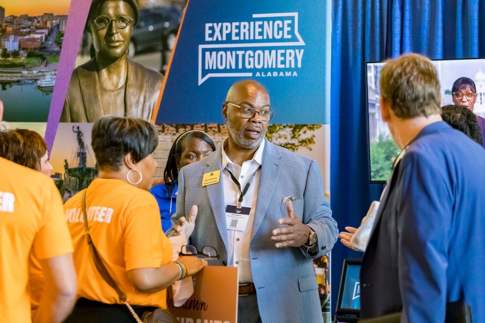 Professional speaker engaging with attendees wearing orange shirts at Experience Montgomery event exhibition.