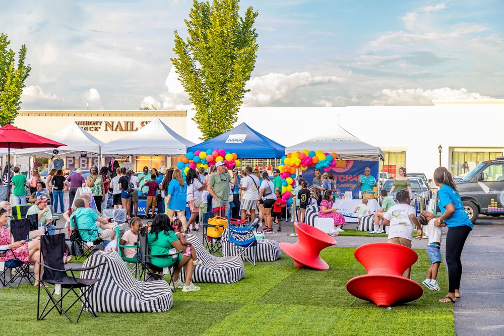 Outdoor festival scene with crowd enjoying food and activities under colorful tents and umbrellas.