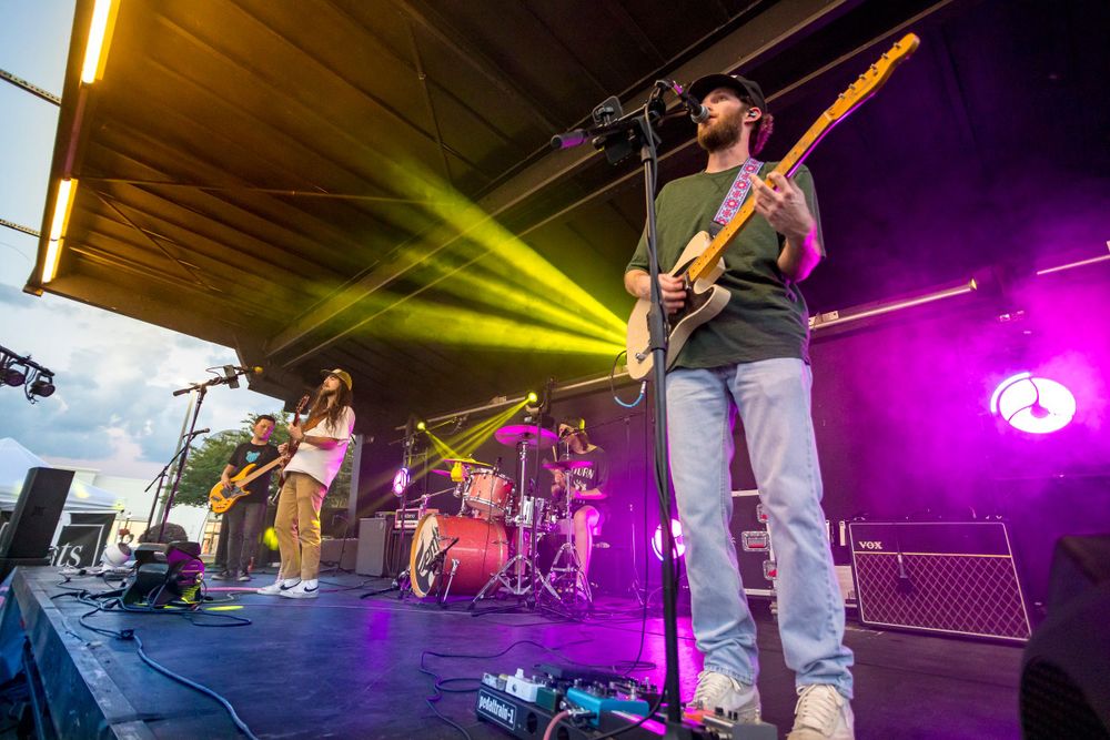Musicians performing on stage with colorful lighting effects at an outdoor concert.