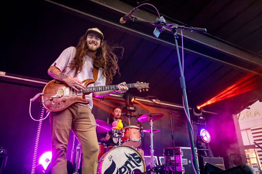 Guitarist performing under vibrant purple and red stage lights.