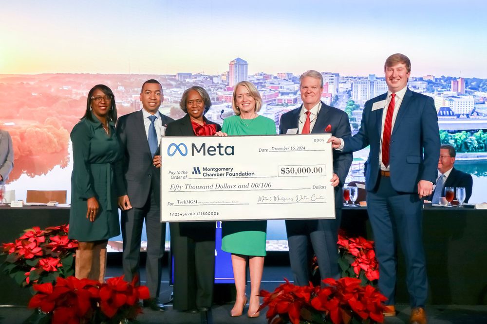 Group presents oversized Meta check donation during formal ceremony with city backdrop.