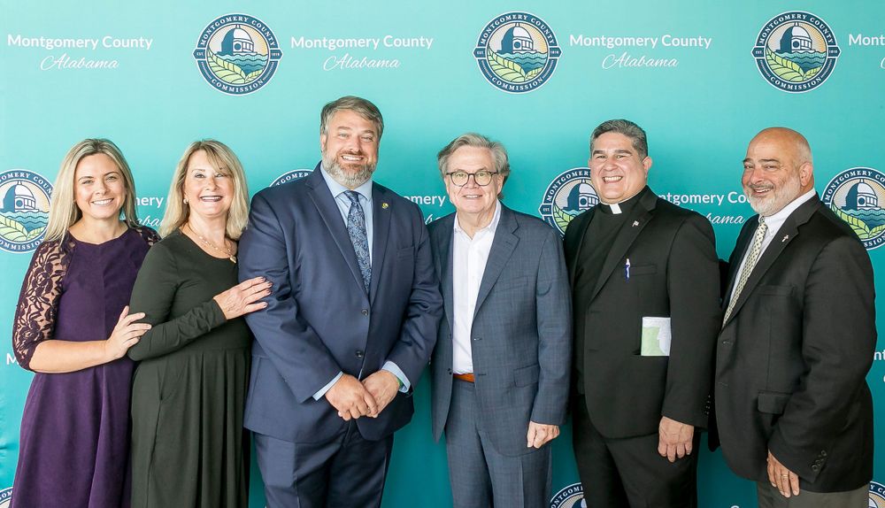 Professional group poses for photo against teal backdrop with organizational logos.