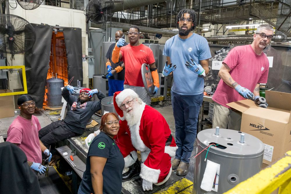 Group of volunteers and Santa Claus sort donations and packages in warehouse setting.