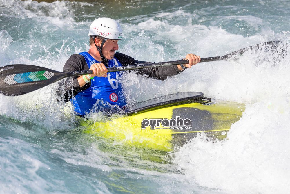 Kayaker in a yellow Pyranha boat paddling through white water rapids while wearing blue safety gear.