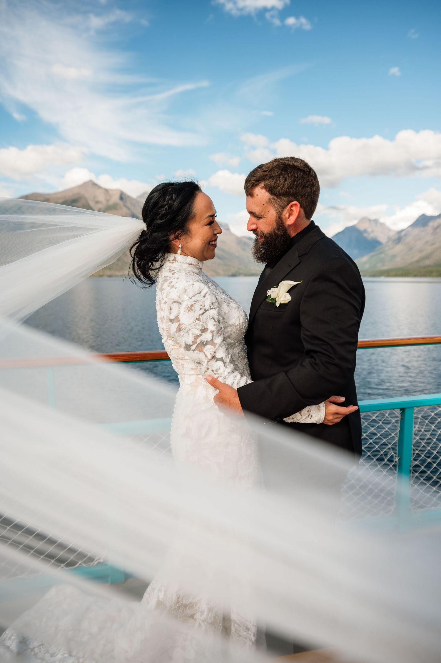 A couple embraces in a romantic wedding moment against a stunning mountain backdrop in a golden meadow at sunset.