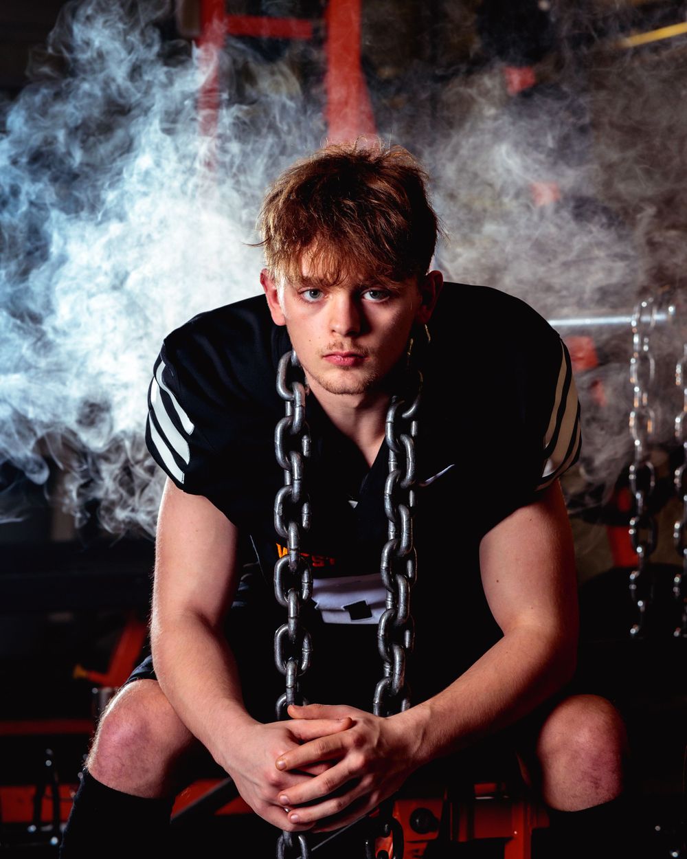A West Valley Senior in a black Football Jersey and shorts sits with a chain, enjoying a moment during his Senior Session.