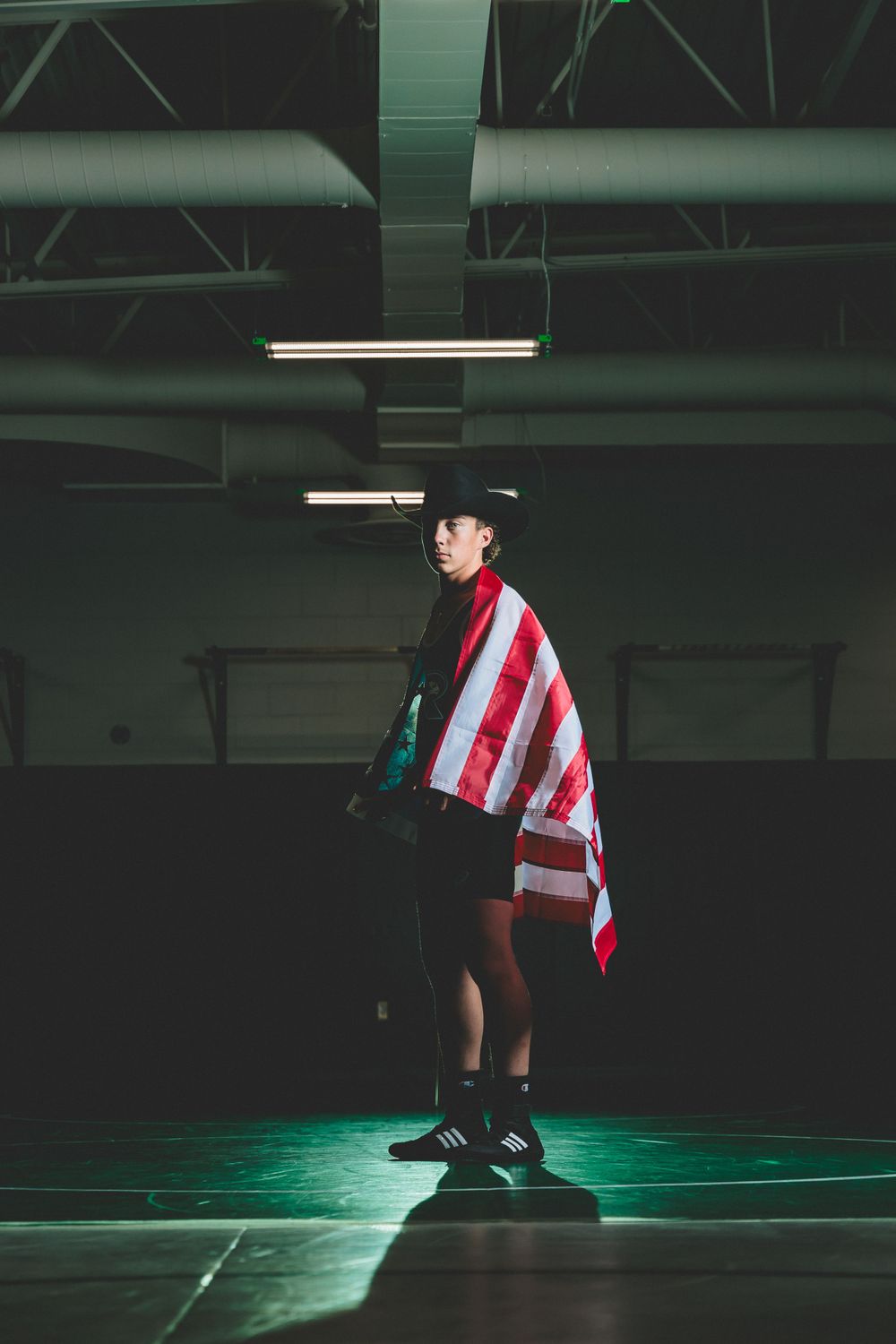 High School Wrestler stands on a dimly lit mat, draped in an American flag, exuding confidence and determination