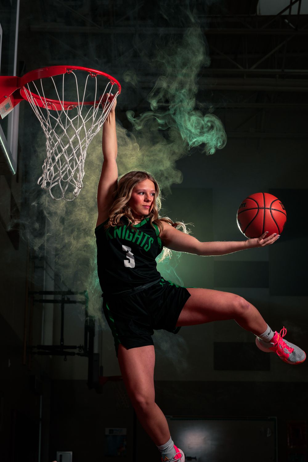 A East Valley Athlete in a striking black and green basketball uniform soars through the air, executing a powerful dunk.