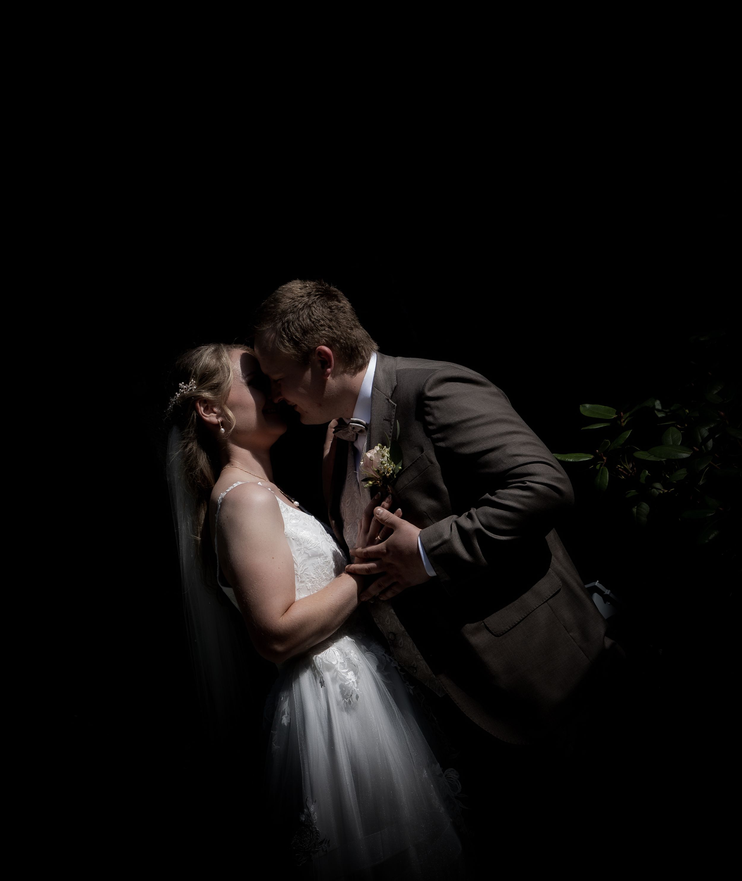 Bride and groom share intimate kiss in dramatic dark spotlight wedding portrait.