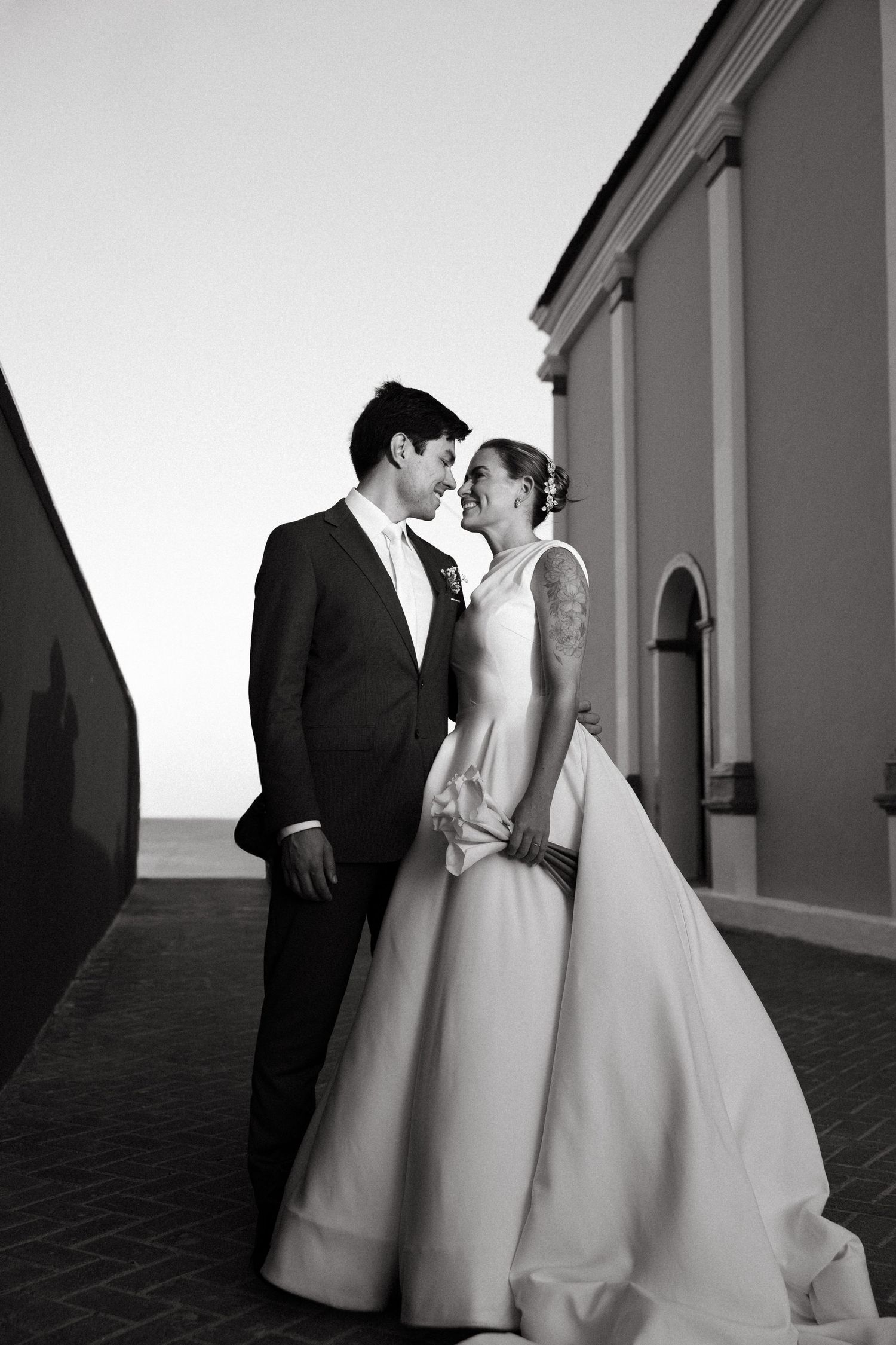 Black and white photo of a bride and groom sharing a romantic moment outside a historic building on their wedding day.