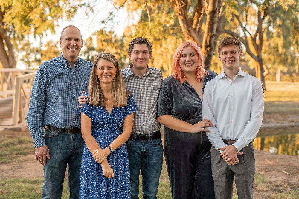 A multi-generational family poses together outdoors at sunset with trees in the background.