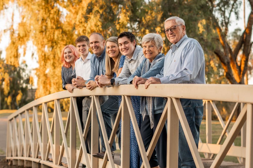 Family members leaning against railing of wooden bridge with autumn trees glowing in background light.