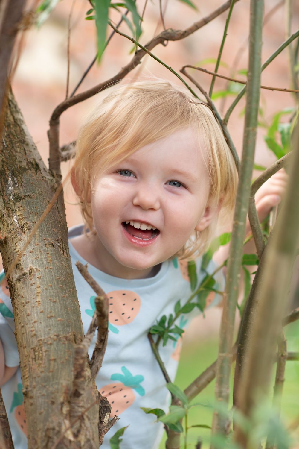 A little girl smiling whilst peeking her head out between a tree