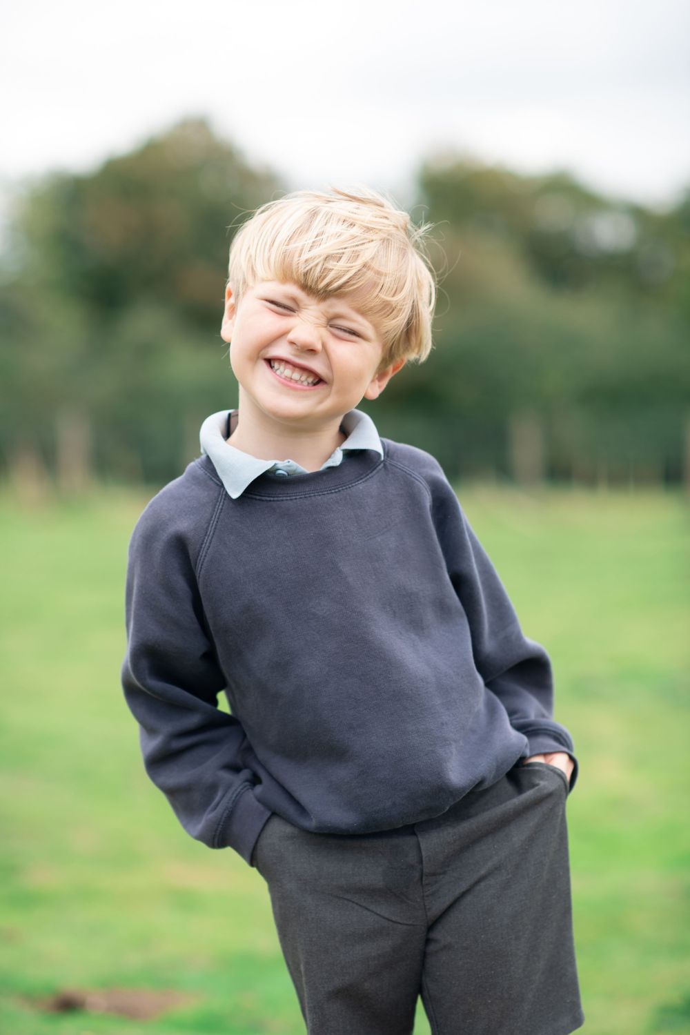 A young boy with a huge smile on his face wearing his school uniform for a natural school photo.