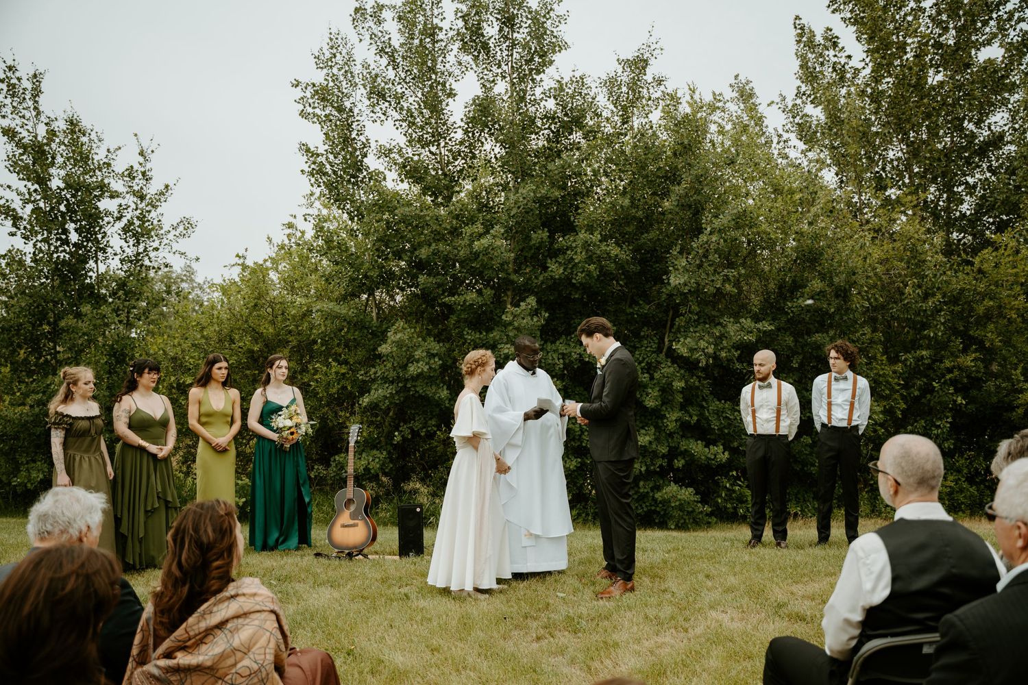 People in vintage attire gather in a green orchard setting for a formal group photograph.