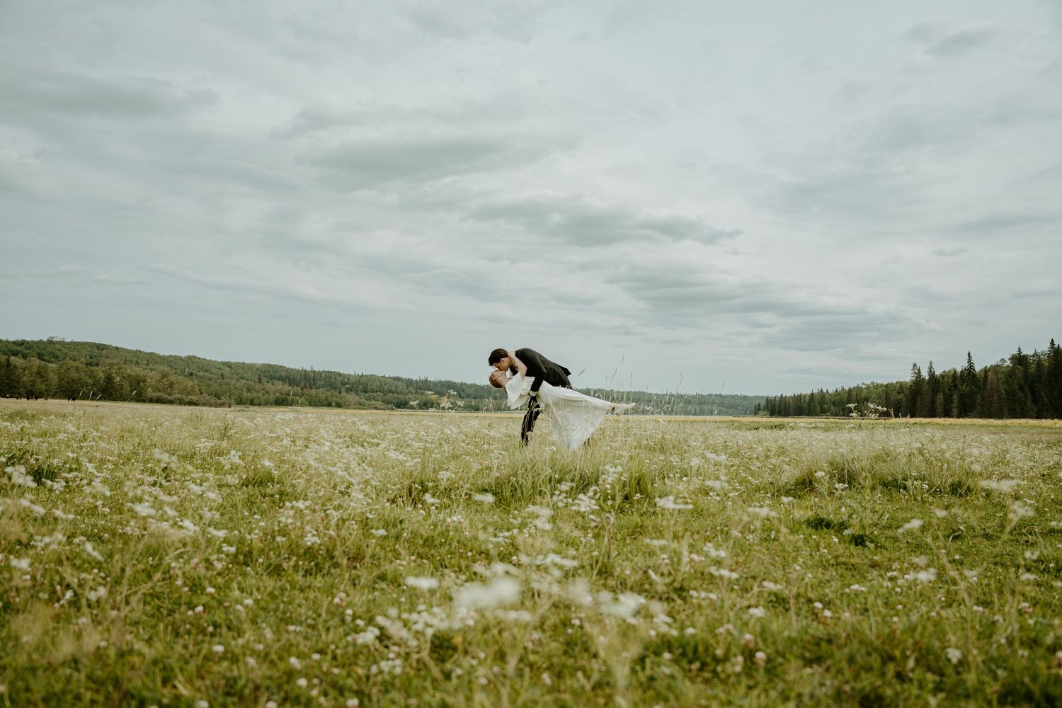 A person stands alone in a vast green meadow under cloudy skies creating a serene rural landscape.