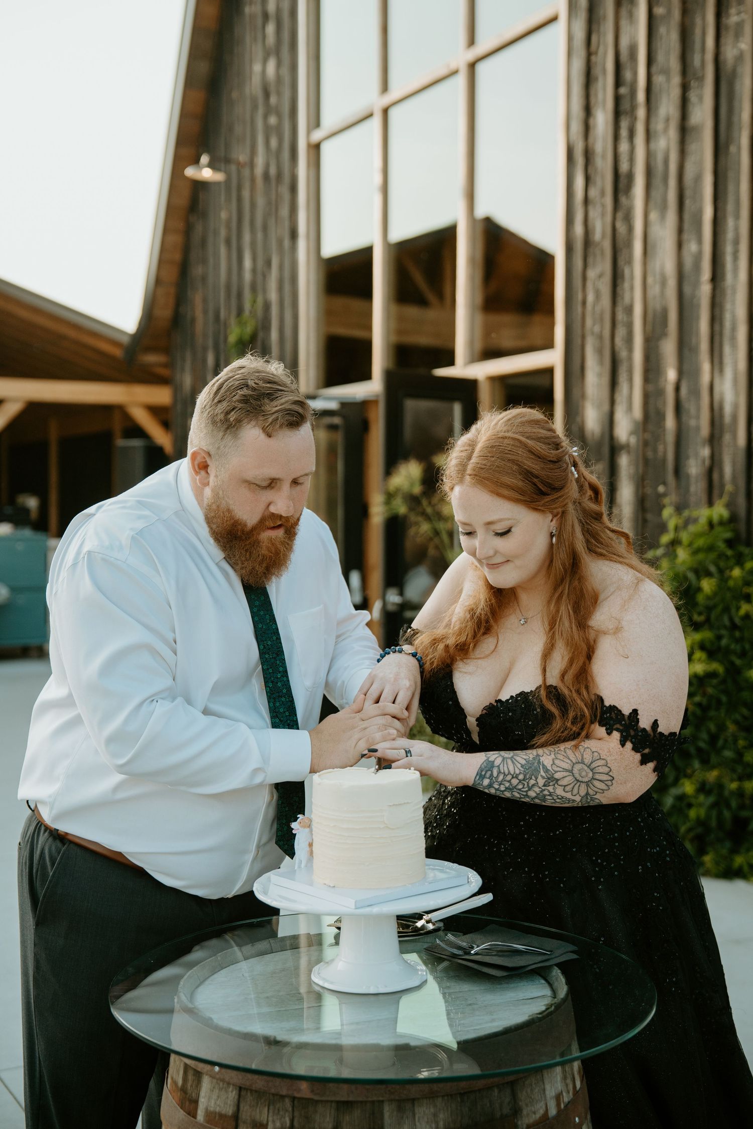 A couple sharing a sweet moment while cutting their wedding cake together at a rustic venue.