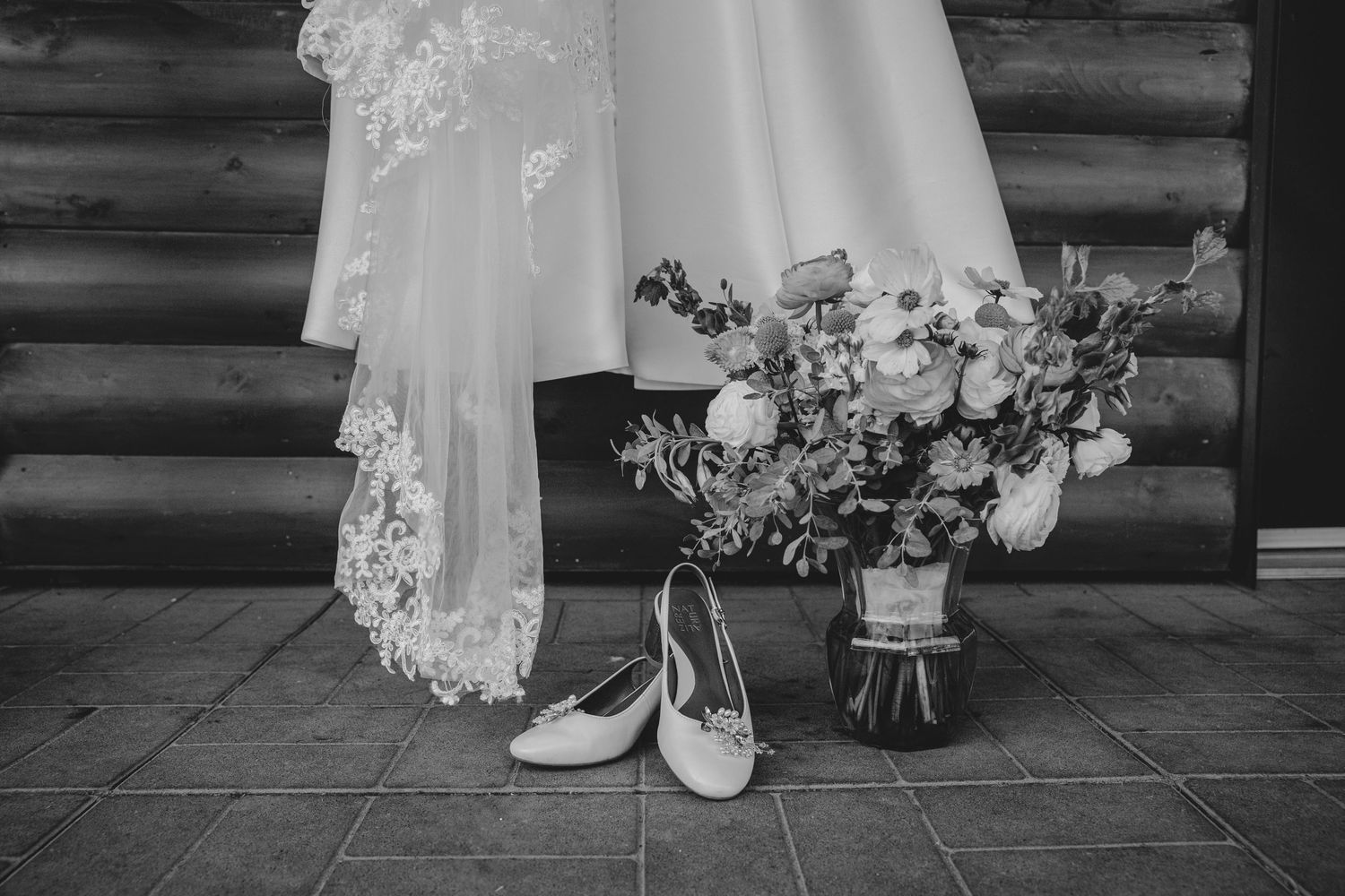 A black and white wedding photo series showing dress details, floral arrangements and bridal accessories against rustic wood walls.