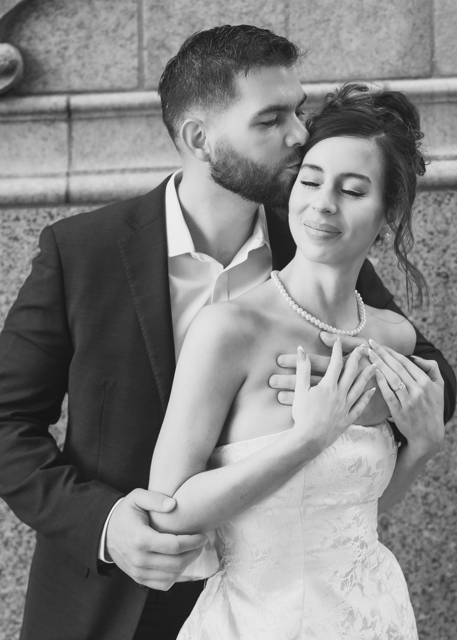 man in black suit coat embracing woman with her eyes closed and kissing her forehead