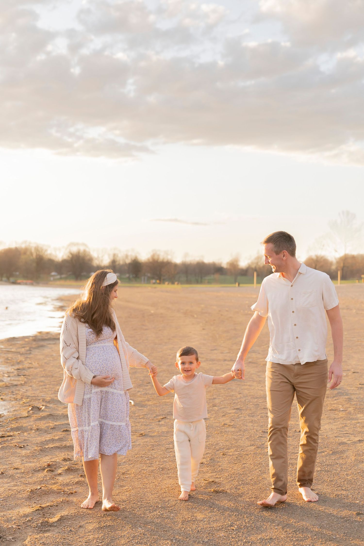 family of three with a pregnant mom walking along the sand beach at Stoney Creek metropark