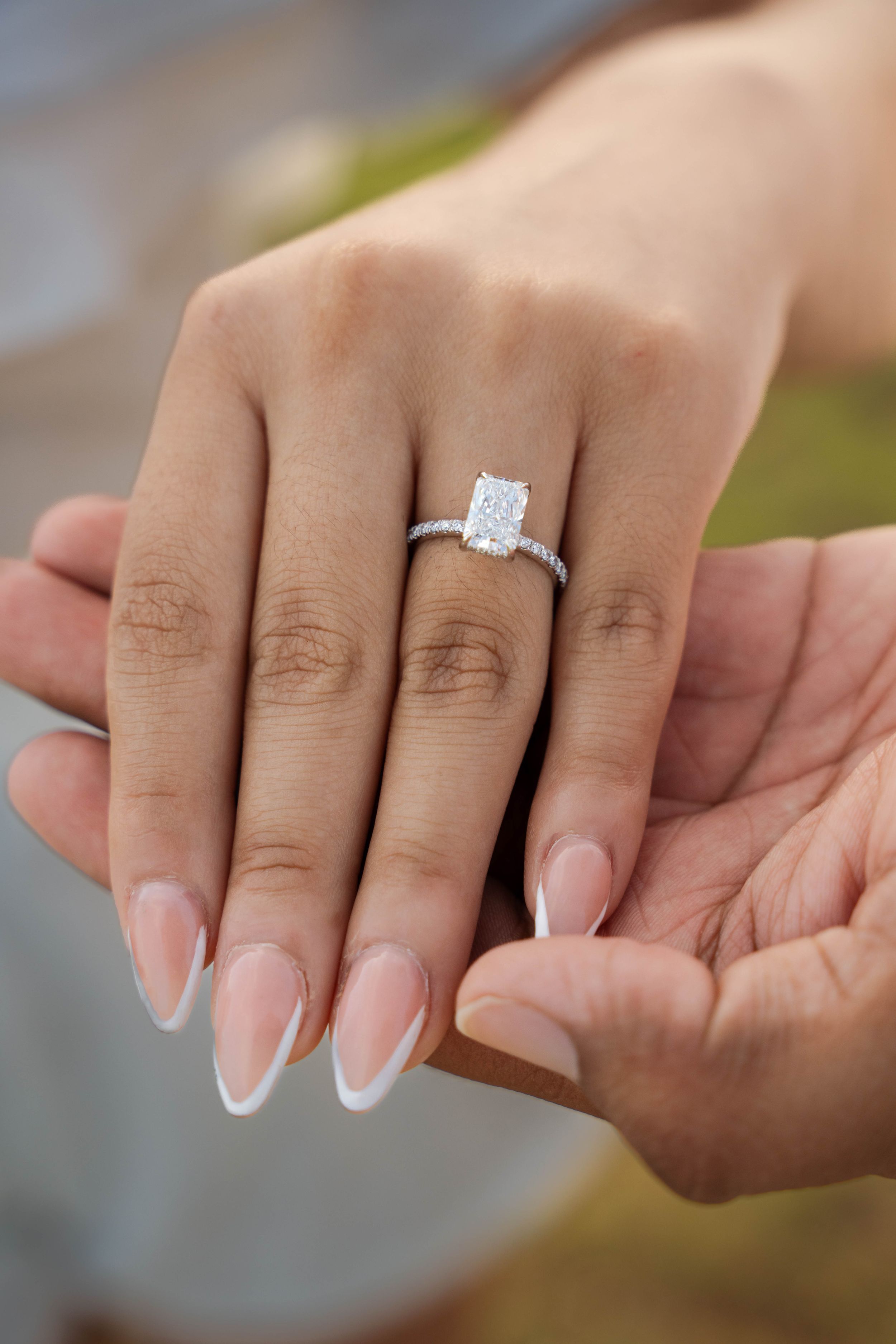 Close-up of an emerald cut diamond engagement ring on a manicured hand with French tips.